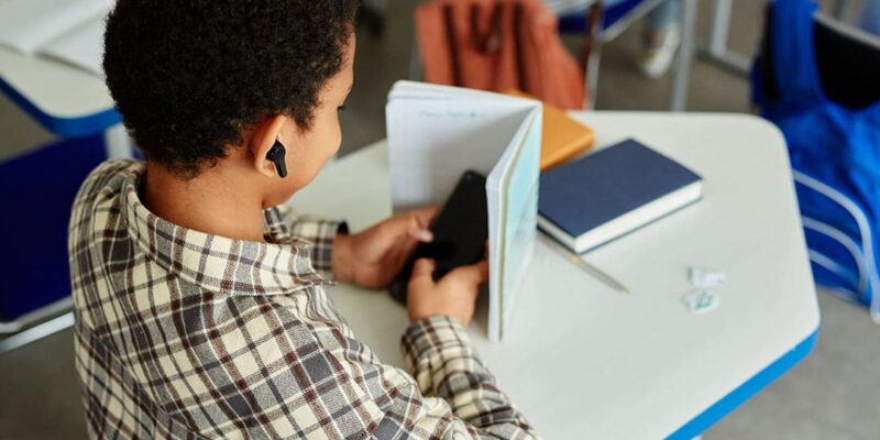 Photo illustrant l'impact du téléphone sur la concentration avec un élève utilisant son smartphone caché derrière un cahier durant le cours.