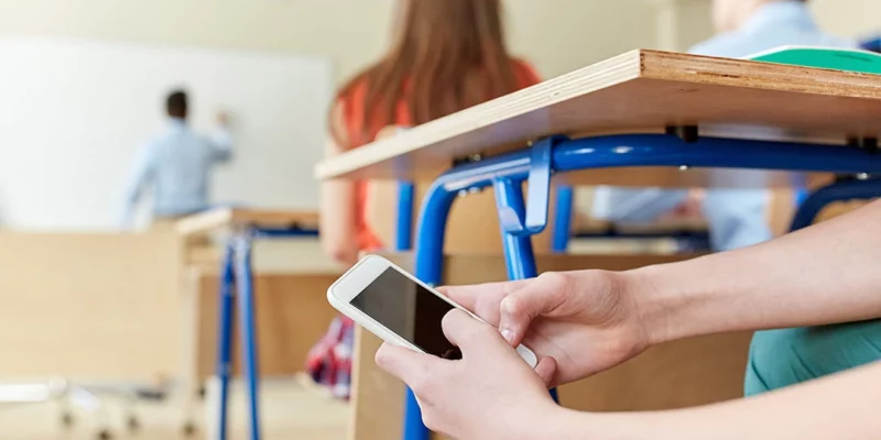 Un jeune étudiant utilise son téléphone discrètement pour envoyer un SMS pendant les cours